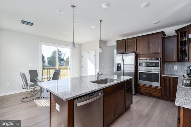 kitchen with decorative backsplash, appliances with stainless steel finishes, sink, light hardwood / wood-style floors, and hanging light fixtures