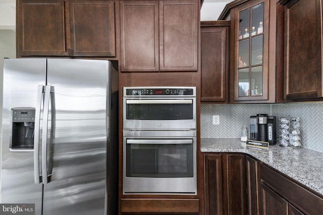 kitchen featuring light stone countertops, appliances with stainless steel finishes, tasteful backsplash, and dark brown cabinets