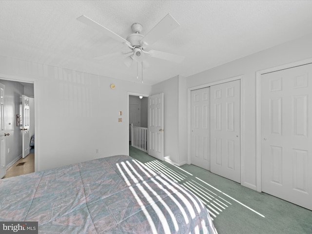 bedroom with carpet, a textured ceiling, ceiling fan, and multiple closets