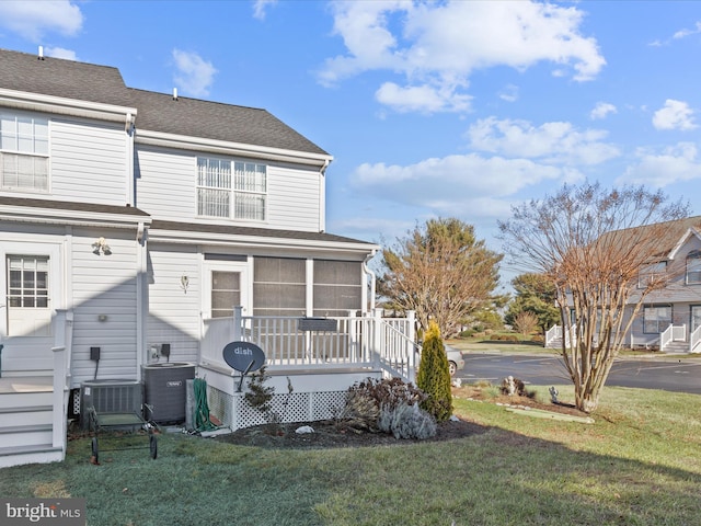 back of property with a sunroom, central air condition unit, and a lawn