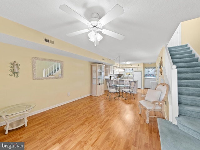 living room featuring ceiling fan, light hardwood / wood-style flooring, and a textured ceiling