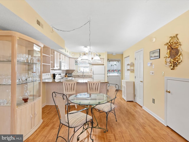 dining space featuring light wood-type flooring, a notable chandelier, and sink