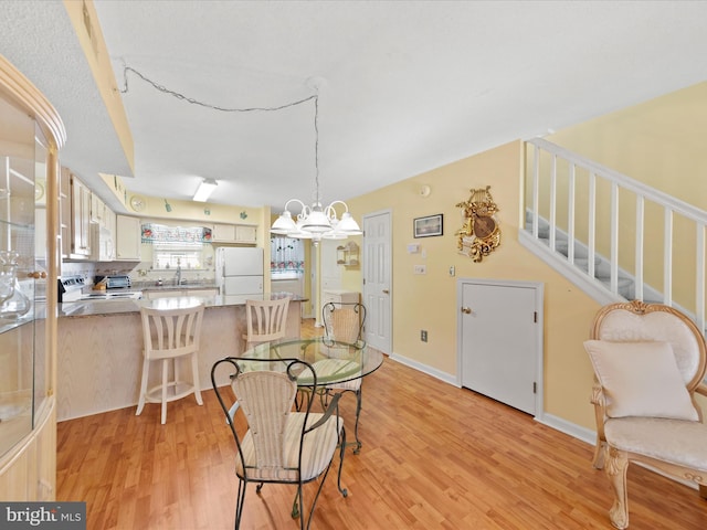 dining area with sink, a notable chandelier, and light wood-type flooring