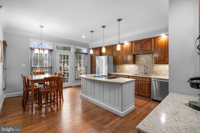 kitchen with sink, light stone counters, hanging light fixtures, appliances with stainless steel finishes, and an island with sink