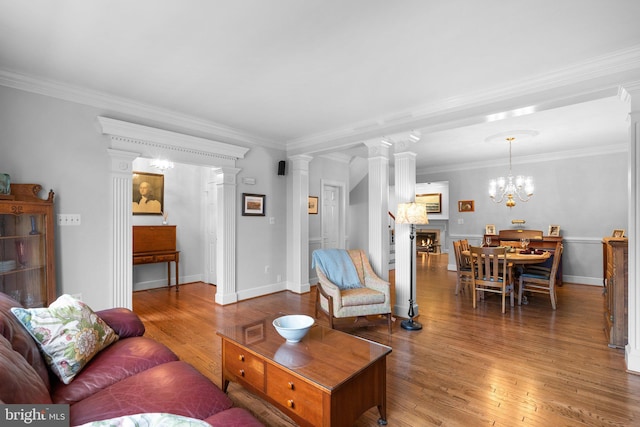 living room with crown molding, wood-type flooring, a chandelier, and ornate columns