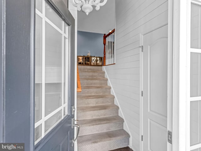 staircase with wooden walls and an inviting chandelier