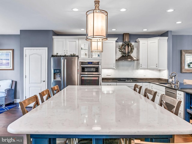 kitchen featuring white cabinetry, sink, hanging light fixtures, wall chimney range hood, and appliances with stainless steel finishes