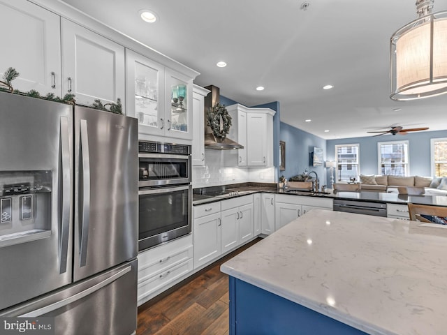 kitchen featuring pendant lighting, white cabinets, wall chimney range hood, sink, and appliances with stainless steel finishes