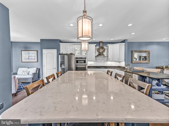 kitchen with white cabinetry, wall chimney exhaust hood, dark stone countertops, pendant lighting, and appliances with stainless steel finishes