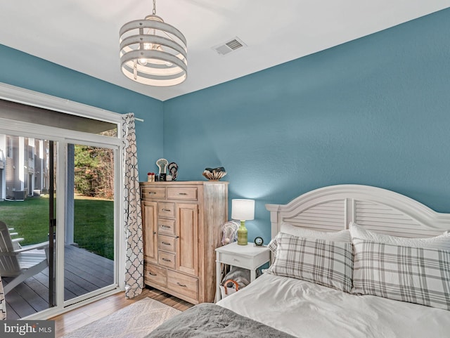 bedroom featuring access to exterior, light hardwood / wood-style floors, and a chandelier