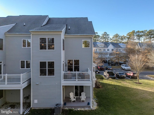 back of property featuring a balcony, central AC, and a lawn