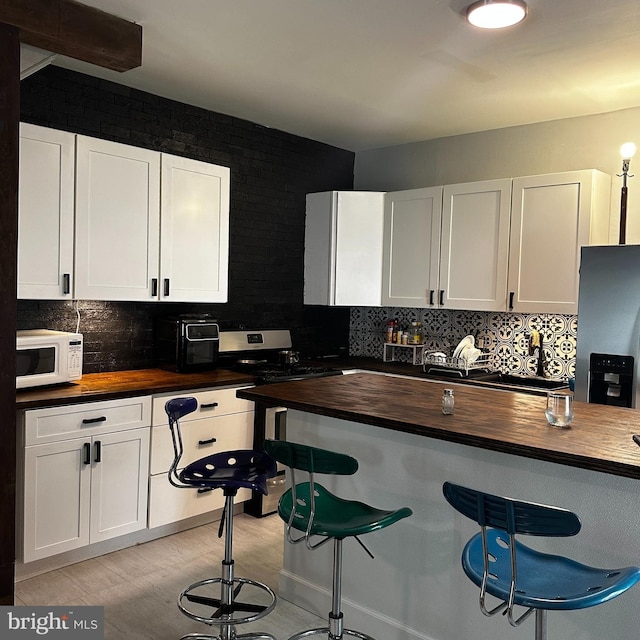 kitchen featuring appliances with stainless steel finishes, light wood-type flooring, butcher block countertops, and white cabinetry