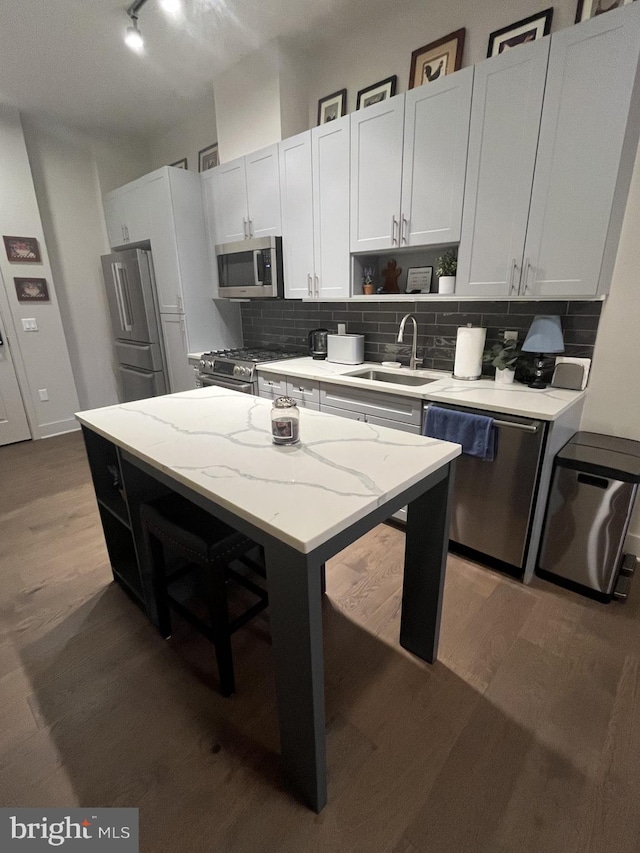 kitchen featuring a center island, high end appliances, sink, light stone counters, and white cabinetry