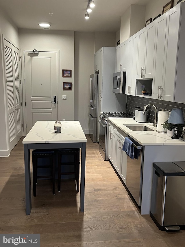 kitchen featuring sink, stainless steel appliances, light stone counters, light hardwood / wood-style flooring, and white cabinets