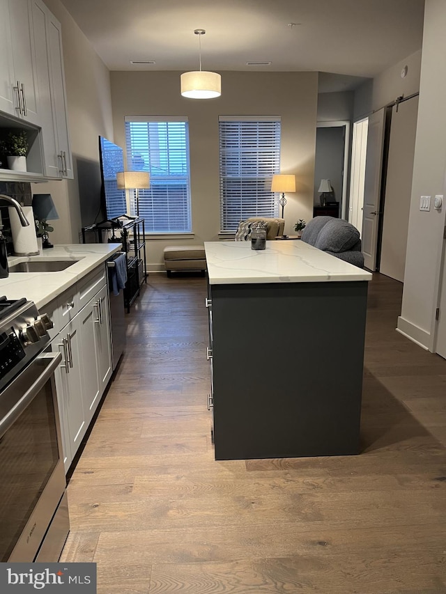 kitchen with a center island, decorative light fixtures, light hardwood / wood-style floors, light stone counters, and stainless steel appliances