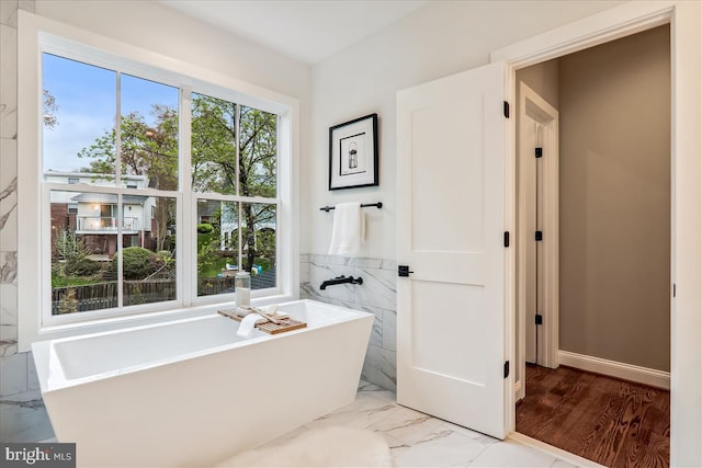 bathroom with marble finish floor and a freestanding bath