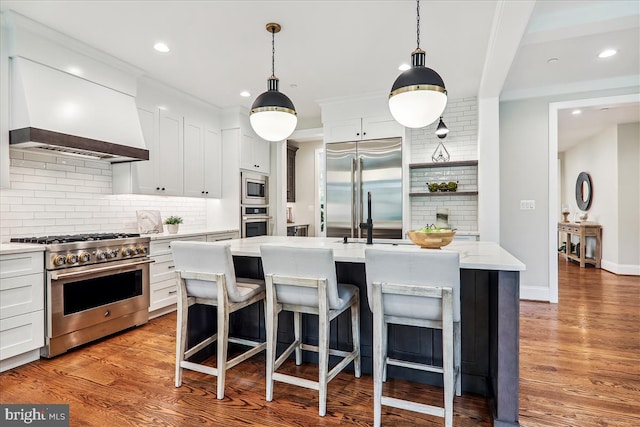 kitchen with premium range hood, hanging light fixtures, light wood-style flooring, and built in appliances