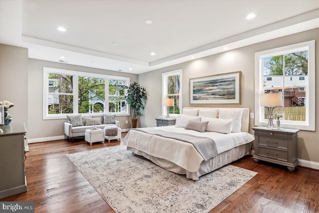 bedroom featuring dark wood-style floors, baseboards, multiple windows, and a tray ceiling