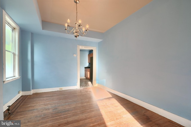 empty room with wood-type flooring, a raised ceiling, and a notable chandelier