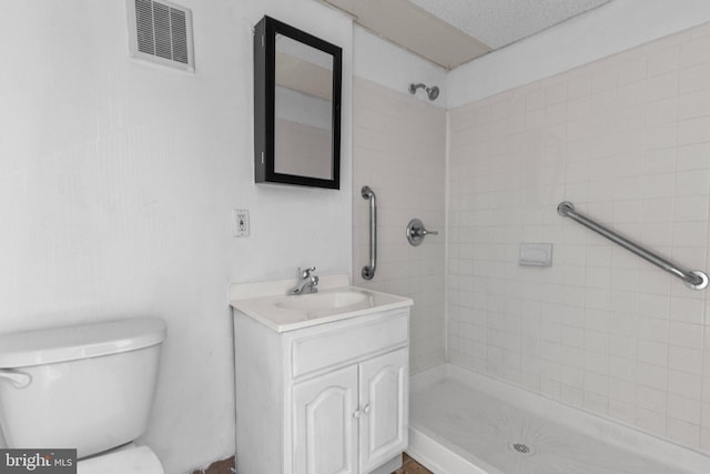 bathroom featuring a tile shower, vanity, a textured ceiling, and toilet