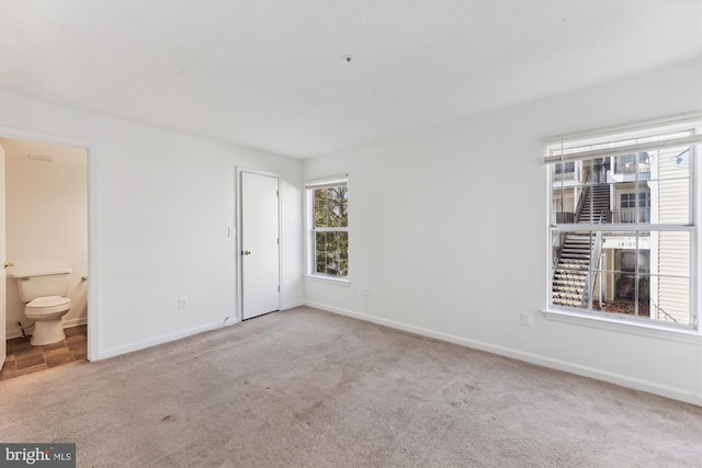 unfurnished bedroom featuring ensuite bath and light colored carpet