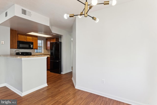 kitchen featuring decorative backsplash, kitchen peninsula, a textured ceiling, black appliances, and wood-type flooring