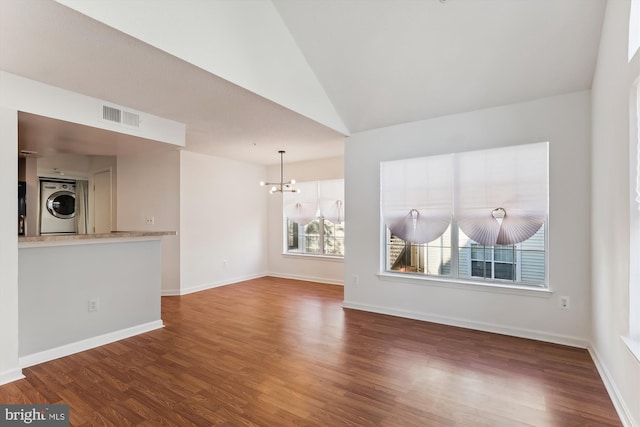 unfurnished living room with stacked washer and dryer, hardwood / wood-style floors, lofted ceiling, and a notable chandelier