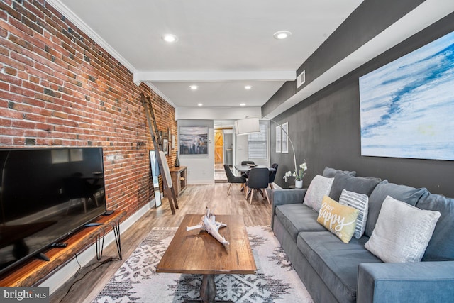 living room with ornamental molding, beamed ceiling, brick wall, and light wood-type flooring