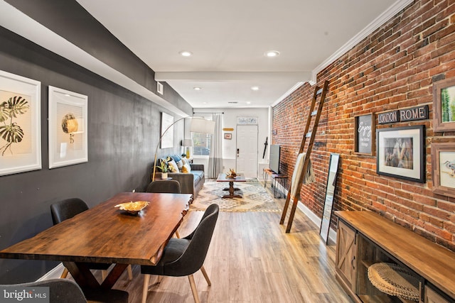 dining space featuring light wood-type flooring, ornamental molding, and brick wall