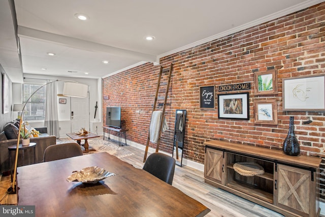 dining space featuring beam ceiling, light hardwood / wood-style floors, ornamental molding, and brick wall