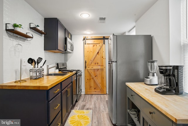 kitchen featuring wood counters, appliances with stainless steel finishes, sink, a barn door, and light hardwood / wood-style flooring