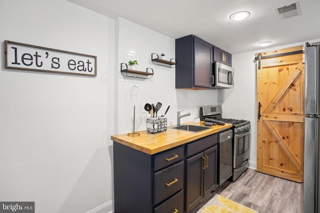 kitchen with sink, stainless steel appliances, a barn door, backsplash, and light hardwood / wood-style floors