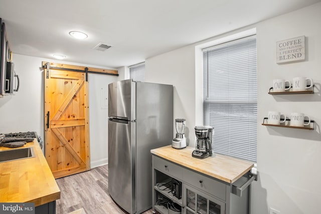 kitchen with gray cabinetry, a barn door, light hardwood / wood-style floors, and appliances with stainless steel finishes