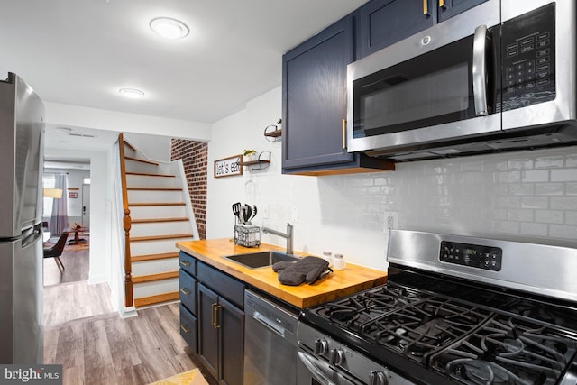 kitchen with blue cabinetry, sink, stainless steel appliances, wooden counters, and light hardwood / wood-style floors