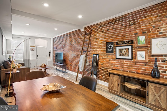 dining space featuring light hardwood / wood-style flooring, beamed ceiling, brick wall, and ornamental molding