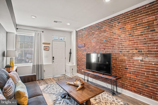 living room with light hardwood / wood-style floors, ornamental molding, and brick wall