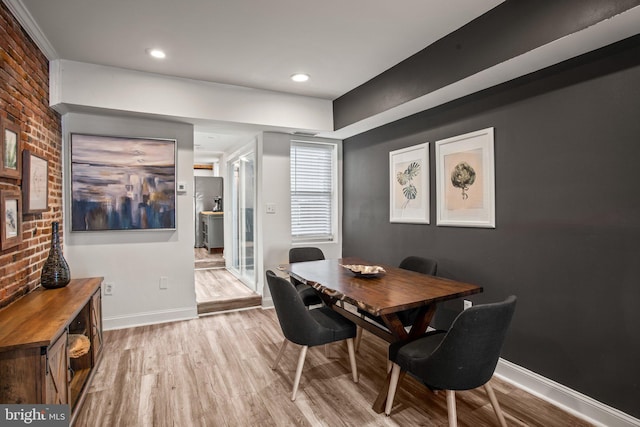 dining room featuring brick wall and light hardwood / wood-style flooring