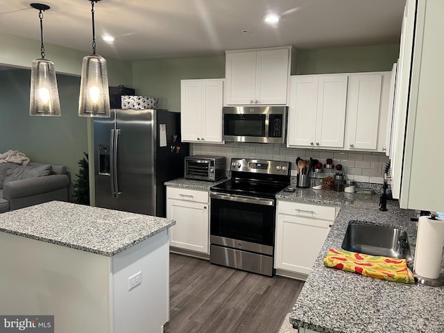 kitchen with white cabinets, dark hardwood / wood-style floors, light stone countertops, appliances with stainless steel finishes, and tasteful backsplash