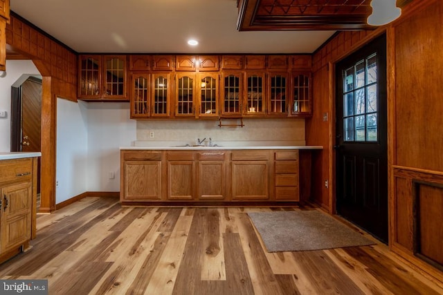 kitchen featuring decorative backsplash, light wood-type flooring, wood walls, and sink