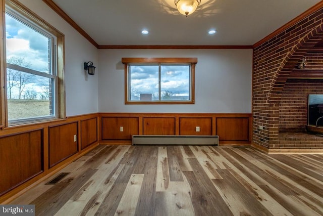 unfurnished living room featuring baseboard heating, a wealth of natural light, light hardwood / wood-style floors, and ornamental molding