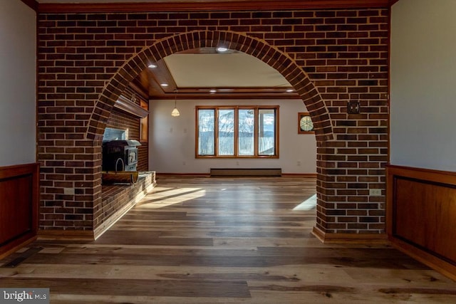 unfurnished living room with baseboard heating, a wood stove, crown molding, and hardwood / wood-style flooring