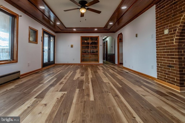 unfurnished living room with a raised ceiling, crown molding, a healthy amount of sunlight, and wood-type flooring