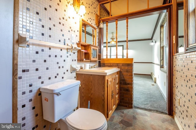 bathroom with a baseboard radiator, toilet, vanity, tile walls, and ornamental molding