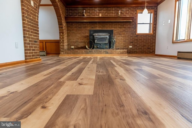 unfurnished living room with a wood stove, crown molding, a baseboard radiator, wood-type flooring, and brick wall