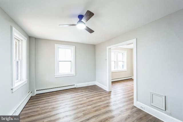 spare room with ceiling fan, light wood-type flooring, and a baseboard heating unit