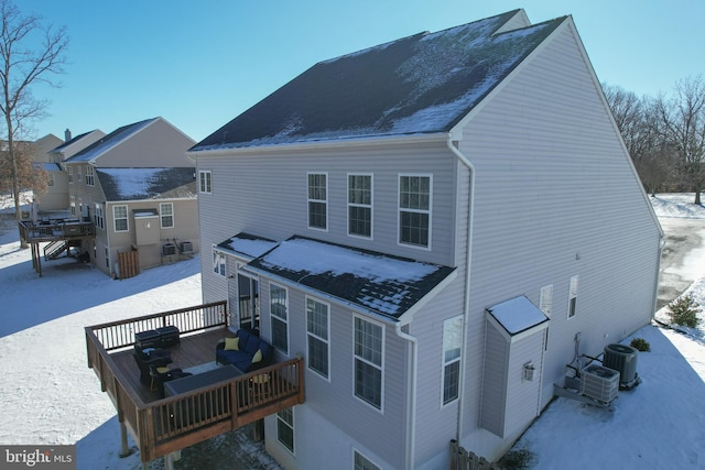 snow covered rear of property with a deck and central AC