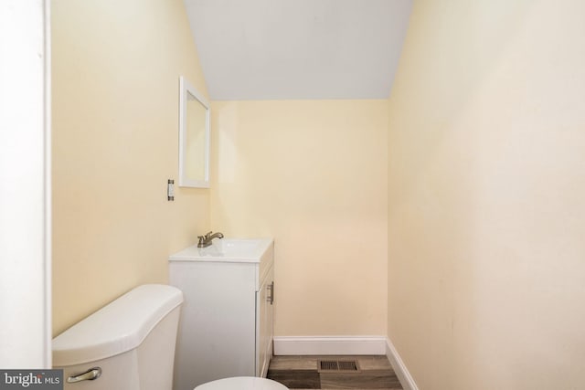 bathroom with hardwood / wood-style floors, vanity, vaulted ceiling, and toilet