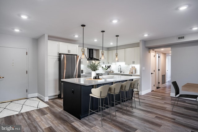 kitchen featuring a center island, wall chimney range hood, dark wood-type flooring, and white cabinetry