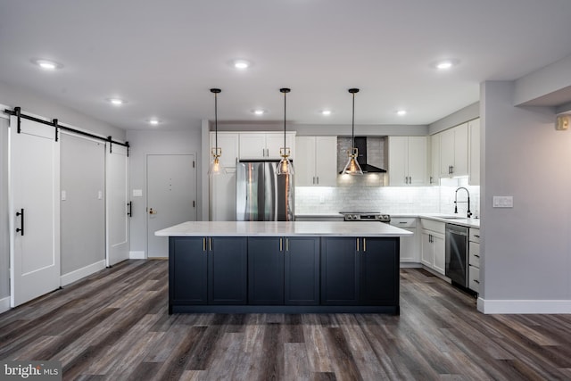 kitchen featuring wall chimney exhaust hood, a barn door, dark hardwood / wood-style floors, appliances with stainless steel finishes, and decorative light fixtures