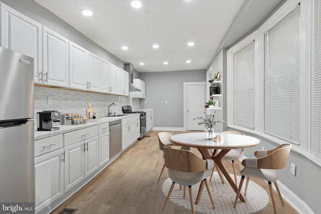 kitchen with white cabinets, appliances with stainless steel finishes, light wood-type flooring, and backsplash